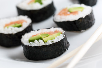 Sushi rolls with salmon, avocado, rice in seaweed and chopsticks on a plate.