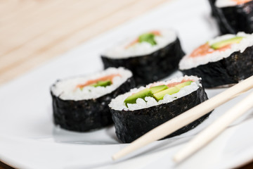 Sushi with salmon, avocado, rice in seaweed and chopsticks on a plate.