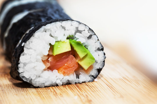 Sushi with salmon, avocado, rice in seaweed and chopsticks on wooden table