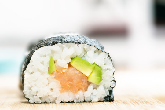 Sushi with salmon, avocado, rice in seaweed and chopsticks on wooden table