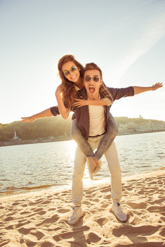 at sunset happy young man piggybacking his girlfriend at the sea