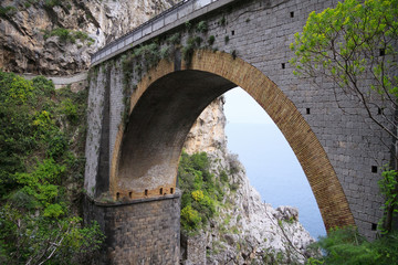 Fototapeta na wymiar Arched bridge between rocks and sea and sky visible beneath it 