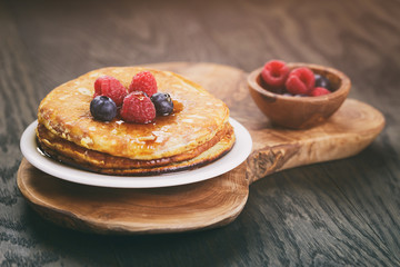 Pancakes with berries on wood table, vintage toned
