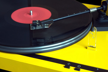 Turntable in yellow case playing a vinyl record with red label. Horizontal photo isolated on black background closeup