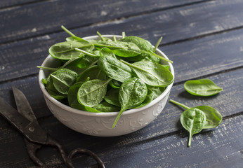 Fresh spinach in a white bowl on a dark wooden background. Healthy food