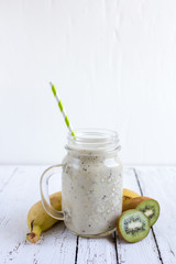 Smoothie with banana, kiwi and milk on white wooden background,