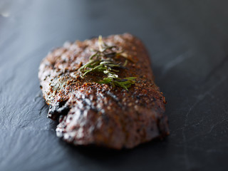 grilled flat iron steak resting on slate slab with rosemary garnish
