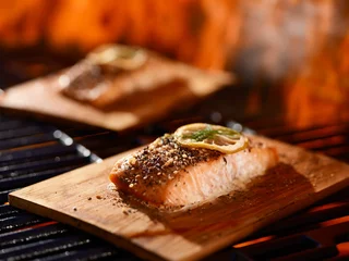 Tuinposter cedar plank salmon with lemon and dill garnish cooking on grill © Joshua Resnick