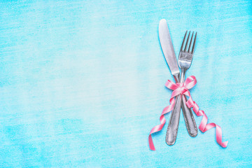 Cutlery set with pink ribbon on light blue background, top view, place for text. Table place setting.