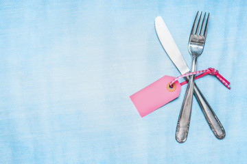 Cutlery set with pink blank tag on light blue background, top view, place for text. Table place setting.