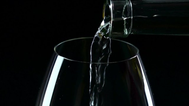 In a large glass of white wine poured, black, closeup, slowmotion