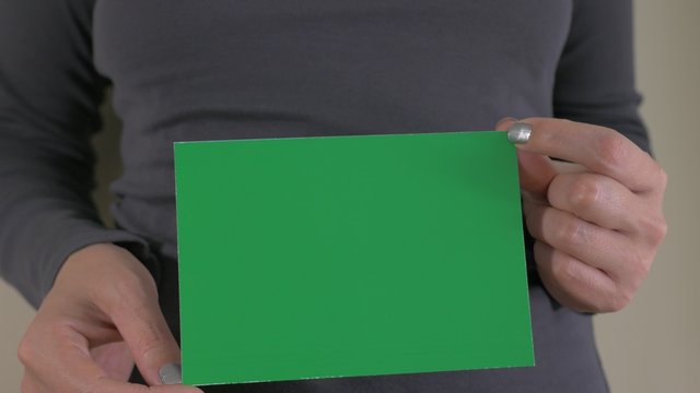 Woman holding in hands green paper screen for chrome key effects while camera tilts 4K 2160p UltraHD footage - Female holding in hands green screen chroma display paper 4K 3840X2160 UHD tilting video 