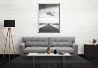Road picture in vertical art frame on wall. Sofa, lamp, plant, glasses, book, coffee on table in...