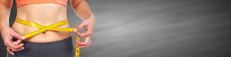 Woman abdomen with measuring tape over black background.