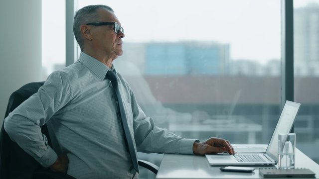 elderly businessman working with computer in modern office. his back is hurts