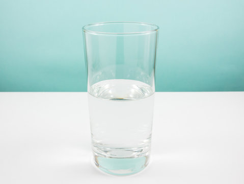 Half empty or half full glass of water on white table. (For positive thinking when see the glass is half full.)