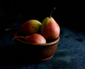 Three ripe pears in the plate on a dark background