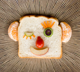 Funny happy winking bread face made with fruit and vegetables on ceramic plate