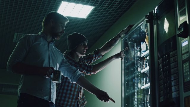 coworkers choosing food in vending machine at night office building