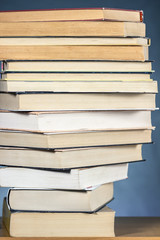 Stack of books placed in stages over a wooden rack, on textured blue background