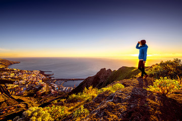 Young female traveler in blue jacket enjoying landscape view on Santa Cruz city on La Palma island in the morning - obrazy, fototapety, plakaty