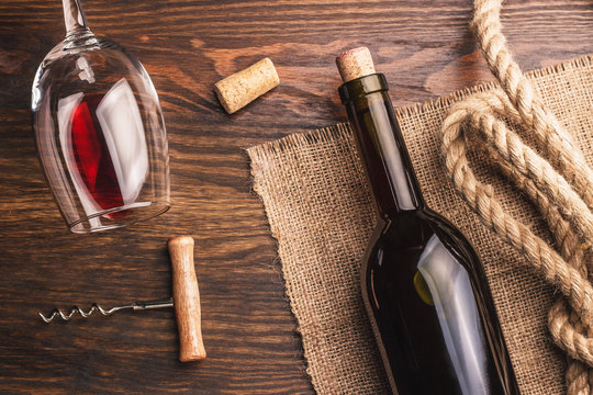 Glass with wine, bottle, corkscrew and burlap, wooden background