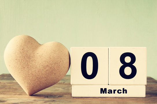image of wooden March 8 calendar, next to white heart on old rustic table. selective focus. vintage filtered and toned
