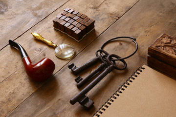 detective concept. Private Detective tools: magnifier glass, old keys, smoking pipe, notebook. top view. vintage filtered image
