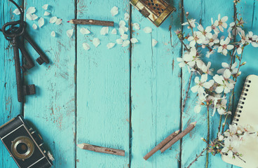 top view image of spring white cherry blossoms tree, blank notebook, old camera on blue wooden table. vintage filtered and toned
