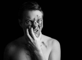 Portrait of angry young man with paint on his face on dark background. Black and white toned.