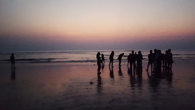 Crowd of silhouette people walking and taking picture with their mobile phones in a beach near sunset.