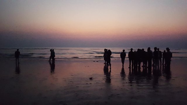 Crowd of silhouette people walking and taking picture with their mobile phones in a beach near sunset.