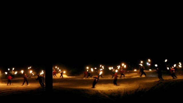 A large group of skiers holding flambeaux torches while skiing and coming down from the mountain at night - travel symbol