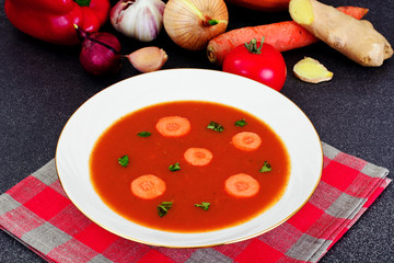 Carrot Tomato Soup in Plate. Behind lie on the soup ingredients,