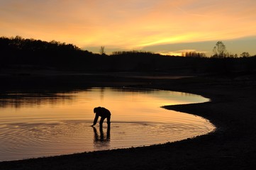 Fototapeta na wymiar Femme ramassant un bâton dans un lac au crépuscule