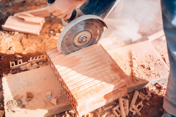 close-up details of worker using angle grinder for cutting bricks on construction site