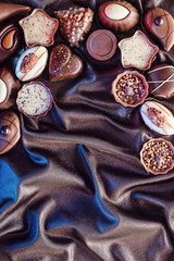 Assorted delicious chocolate pralines background on satin background and blue lights, place for text, product photography for patisserie