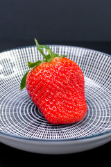 big red strawberry in a plate with white and black stripes, contrast color image with space for text. sophisticated look berries.