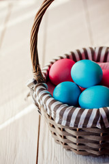 Multicolored Easter eggs in wicker basket on white wooden background