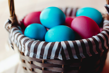 Multicolored Easter eggs in wicker basket on white wooden background