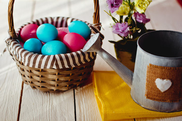 Multicolored Easter eggs in wicker basket on white wooden background