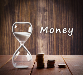 Hourglass with coins on wooden table on wooden background