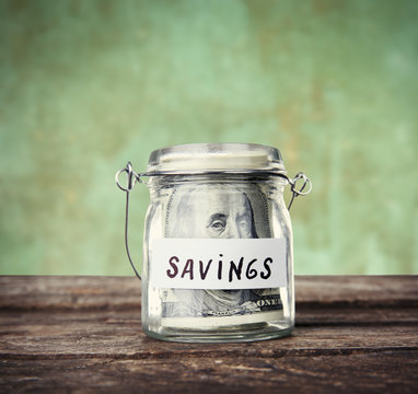 Jar for savings full of coins on wooden background
