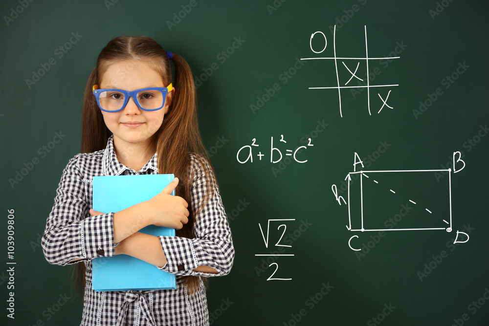 Wall mural Beautiful little girl  near blackboard in classroom