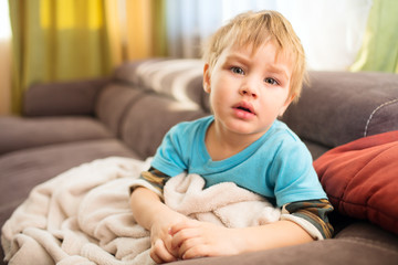 Naklejka premium the sad kid sits under a blanket in the room, an illness 