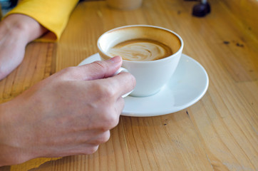 hand holding white coffee cup on wood table in coffee cafe.
