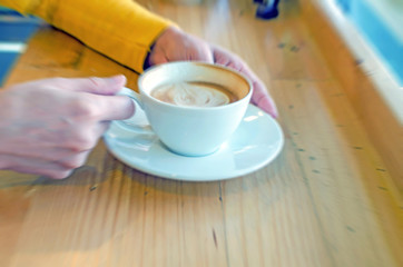 Blurred hand holding white coffee cup on wood table in coffee ca