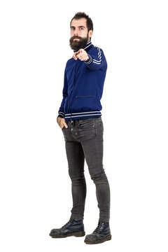 Confident serious hipster in blue tracksuit jacket pointing finger at camera. Full body length portrait isolated over white studio background. 