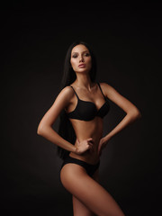 Sexy model with dark straight hair, almond-shaped eyes and tanned skin in the black seamless underwear collection is posing in the studio on the black background