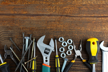 the different forms of screws and a wrench with nuts and many other tools on the wooden brown table